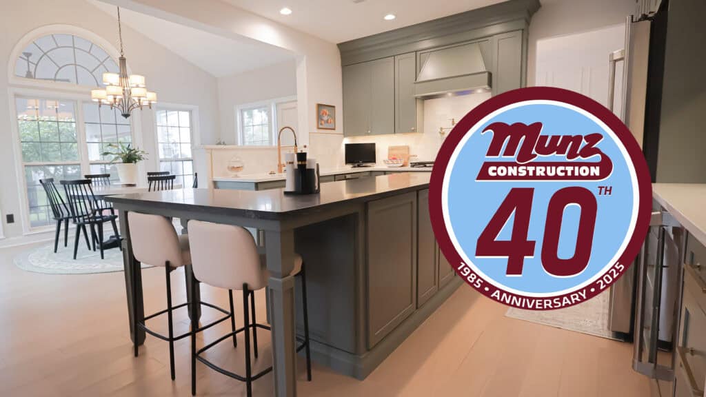Modern kitchen with a large island, two white chairs, dining area with windows, and tips on how to add an in-law suite, plus a Munz Construction 40th Anniversary 1985-2025 logo overlay in the foreground.