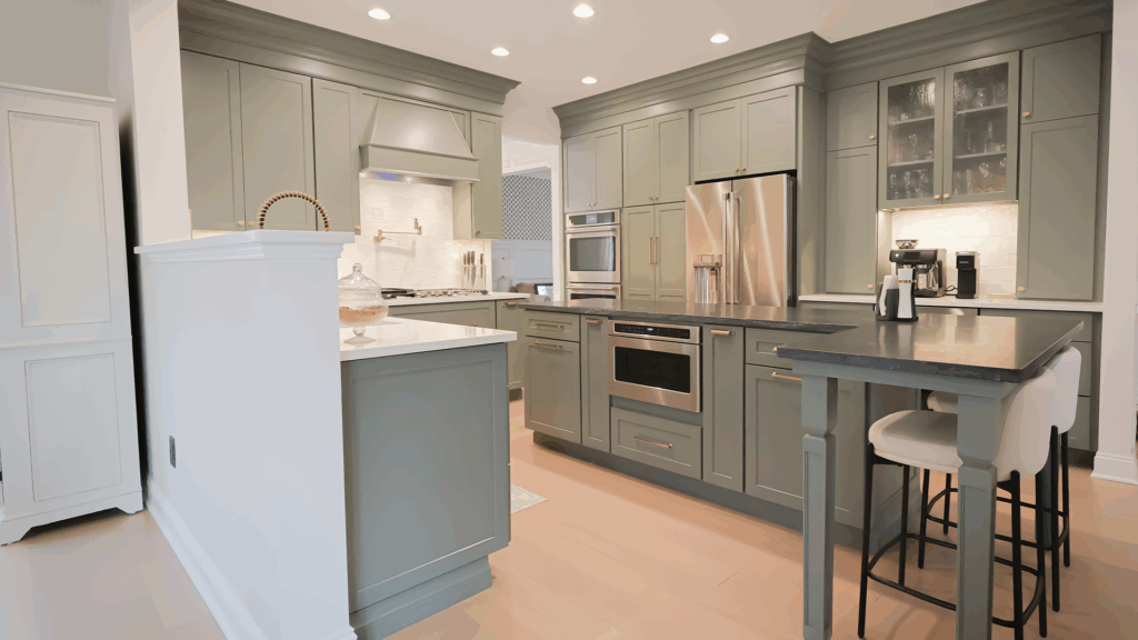 Modern kitchen with sage green cabinets, stainless steel appliances, and a peninsula with two white barstools—perfect inspiration if you’re planning how to build an in-law suite in Pennsylvania. Recessed lighting brightens the sleek, clean space.