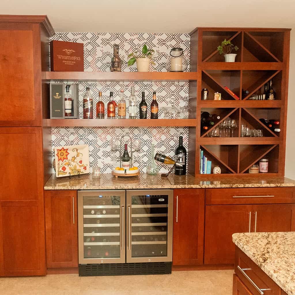 a home bar with wooden cabinets, a granite countertop, wine fridge, wine racks with bottles, liquor bottles on shelves, potted plants, and patterned backsplash in a modern kitchen setting.