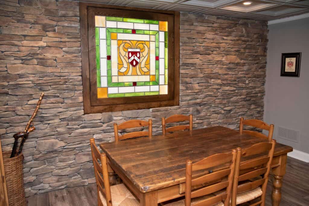 a rustic dining room with a wooden table and six chairs, stone accent wall, stained glass window art, and a basket holding a sword in the corner.