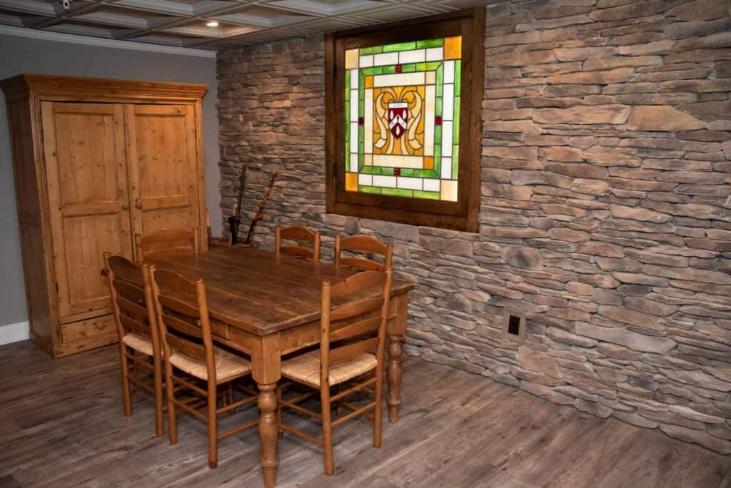 a rustic dining area with a wooden table and six chairs, a wooden cabinet, and a stone accent wall featuring a colorful stained glass window with a lion design. the flooring is wood and the lighting is warm.