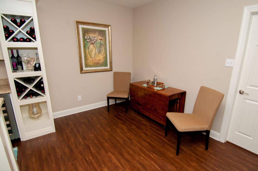 Basement sitting area featuring two beige chairs, a wooden table, and wall art, perfect for relaxing.