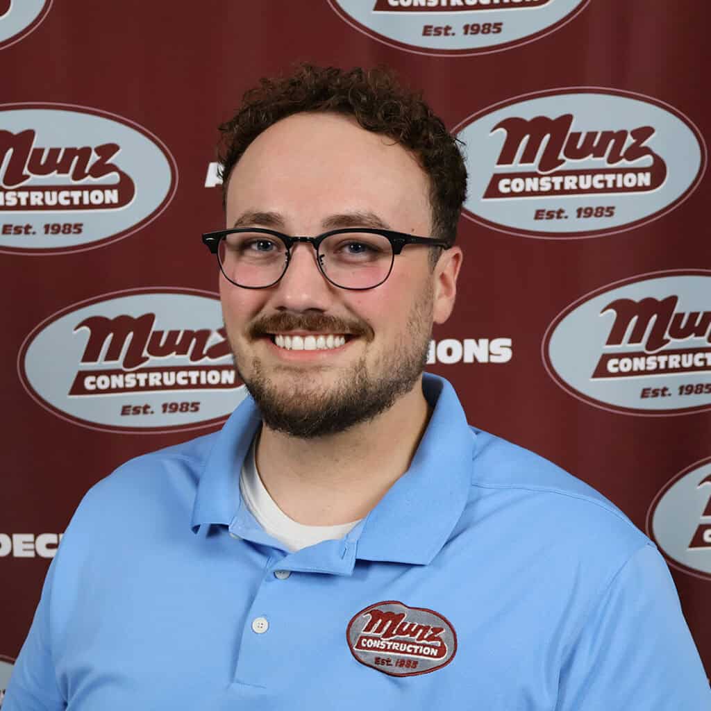 Munz Construction team member smiling in front of company logo background.