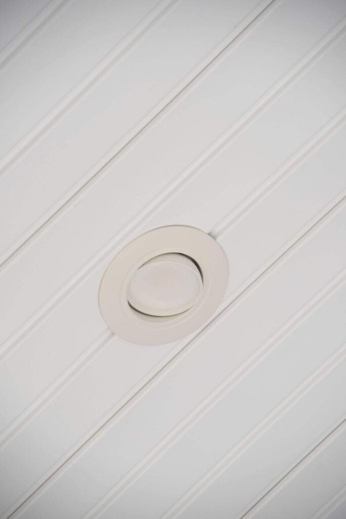 a recessed ceiling light fixture set in a white paneled ceiling, shown from below. the ceiling features evenly spaced vertical grooves creating a striped pattern.