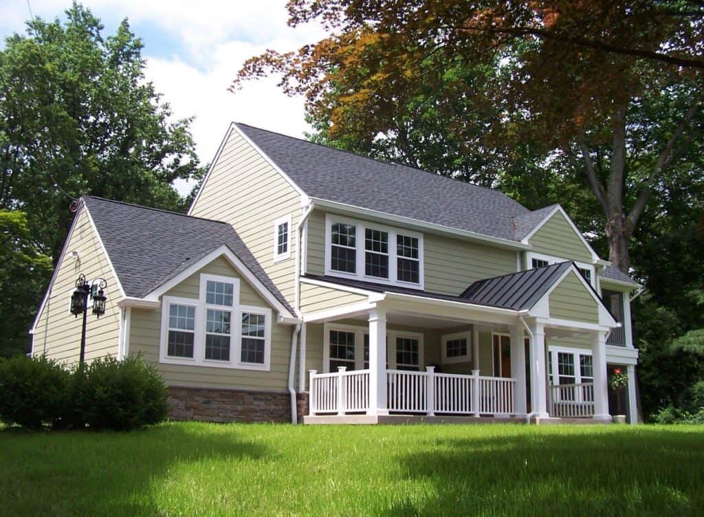 a two story suburban house with light yellow siding, white trim, and a covered front porch, set on a grassy lawn with trees in the background.