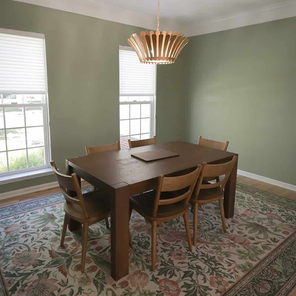 a dining room with sage green walls, a wood table with six matching chairs, a floral patterned rug, two large windows with white blinds, and a modern wooden pendant light fixture. a dining room with sage green walls, a wood table with six matching chairs, a floral patterned rug, two large windows with white blinds, and a modern wooden pendant light fixture.