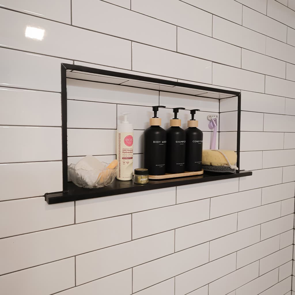 Bathroom shower niche with shampoo, body wash, and soap in a tiled shower.