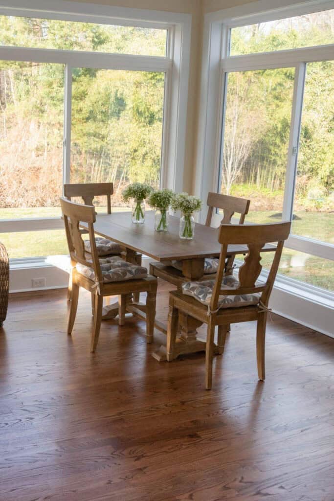 Bright sunroom with wooden dining table and four chairs overlooking nature.