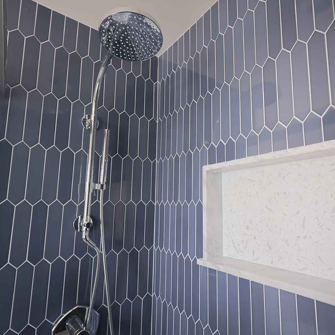 close up of a modern shower with blue hexagonal tile walls, a chrome rainfall showerhead, and a built in white niche for storage. close up of a modern shower with blue hexagonal tile walls, a chrome rainfall showerhead, and a built in white niche for storage.