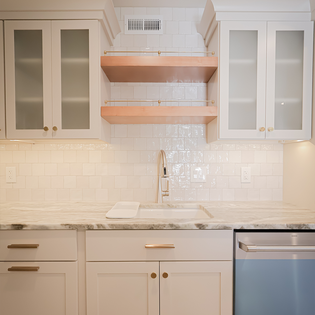 modern kitchen with white cabinets, marble countertop, stainless steel faucet, glass cabinet doors, two wooden shelves, white tile backsplash, and a built in dishwasher on the right. modern kitchen with white cabinets, marble countertop, stainless steel faucet, glass cabinet doors, two wooden shelves, white tile backsplash, and a built in dishwasher on the right.