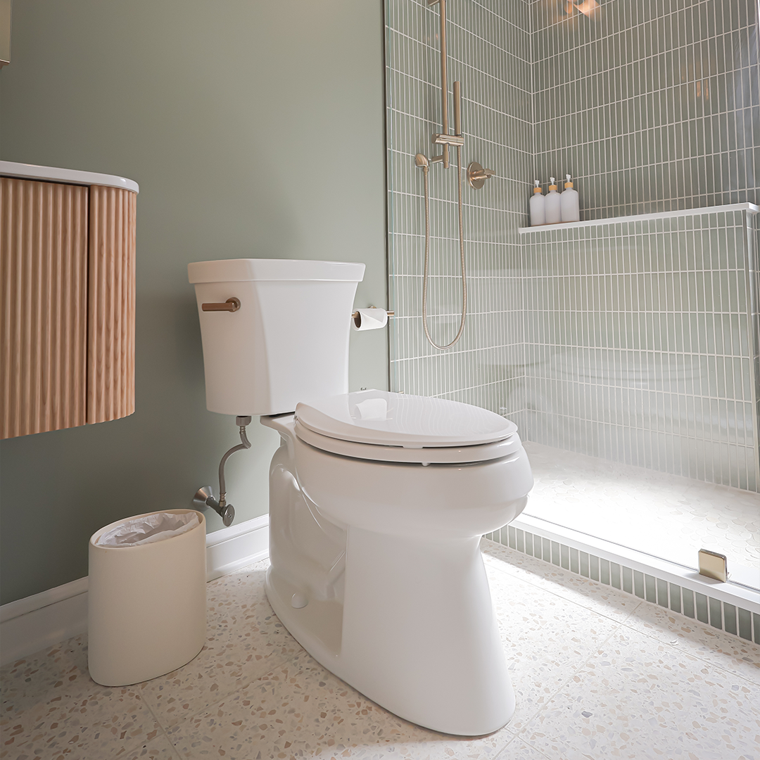 a modern bathroom with a white toilet, a small trash can, a floating vanity, and a glass enclosed shower with vertical green tiles and three bottles on a shelf. a modern bathroom with a white toilet, a small trash can, a floating vanity, and a glass enclosed shower with vertical green tiles and three bottles on a shelf.
