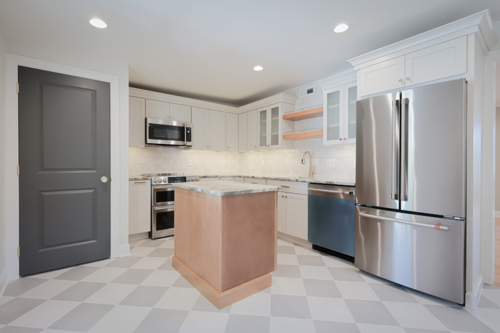 modern kitchen with white cabinets, stainless steel appliances, marble island, checkered floor, and under cabinet lighting. the space is clean, bright, and features a dark door and open wood shelves—an ideal setting to inspire sunroom ideas or seamlessly connect to a four season sunroom for year round natural light.