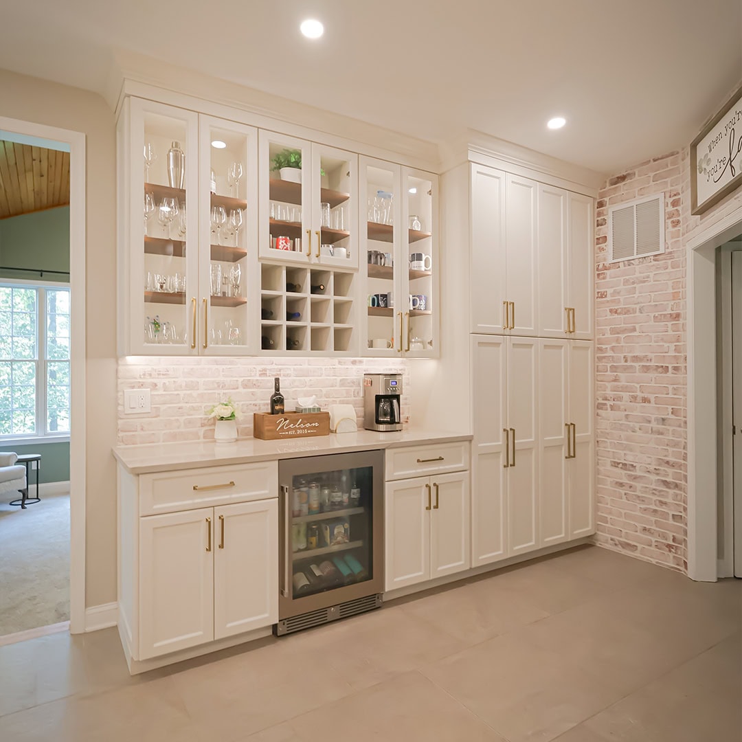 Built-in white kitchen cabinets with glass upper doors, a wine fridge, coffee maker, and white brick backsplash. Built-in white kitchen cabinets with glass upper doors, a wine fridge, coffee maker, and white brick backsplash.