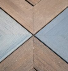 Close-up of four wooden panels meeting at a central point, forming an X-shaped pattern. Each panel is a different shade of brown, gray, or blue, highlighting the wood grain texture.